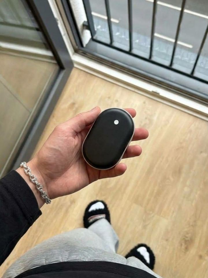Mano sujetando el calentador de manos Calore junto a un balcón
