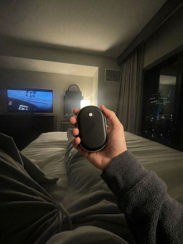Mano sujetando el calentador de manos Calore tumbado en una habitación