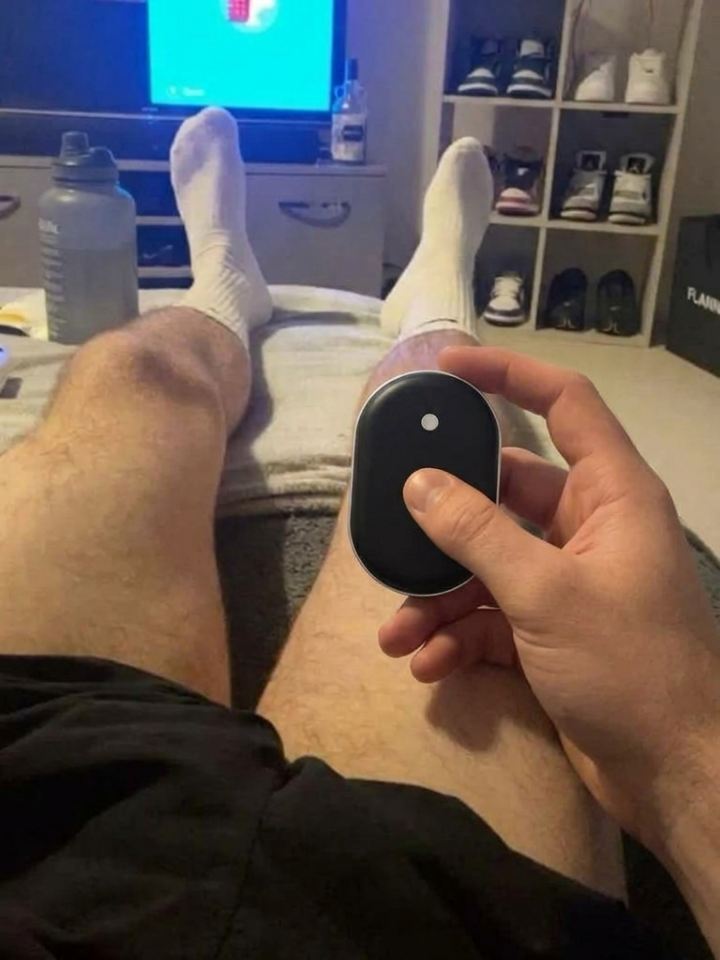 Mano sujetando el calentador de manos Calore con las piernas en alto viendo la tele