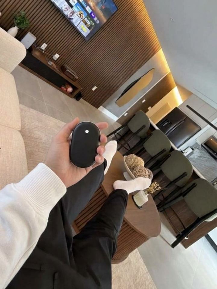 Mano sujetando el calentador de manos Calore en el salón de casa