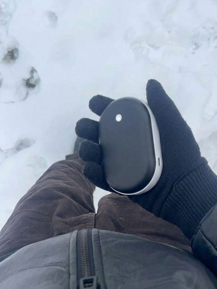 Mano con guante sujetando el calentador de manos Calore sobre la nieve